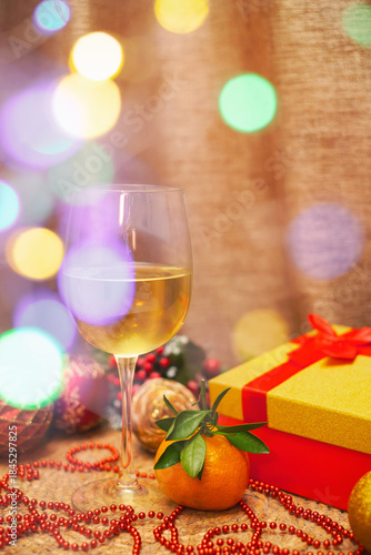 A glass of wine and a tangerine next to a gift in a box with Christmas tree balls