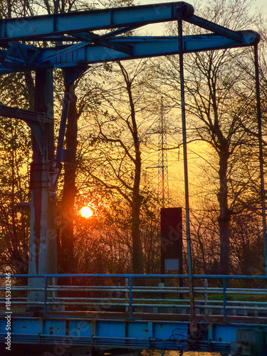 Rijkevorsel, Antwerpse Kempen, Belgium, Bridge silhouette at golden sunset glow, industrial steel structure with weathered railings framed by bare trees, warm orange