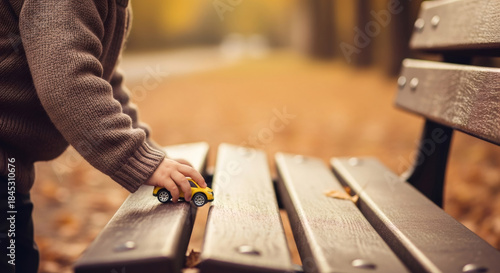 Fototapeta Naklejka Na Ścianę i Meble -  Kid hand playing with yellow toy car on wooden bench. Preschool child having fun with small vehicle game. Autumn playtime concept.