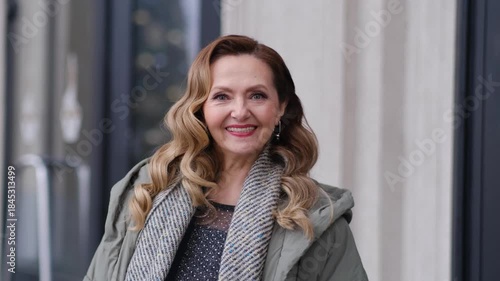 A woman wearing a green coat and a black shirt. She has long hair and is wearing earrings