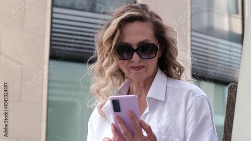 A woman is holding a cell phone and wearing sunglasses. She is looking at the phone
