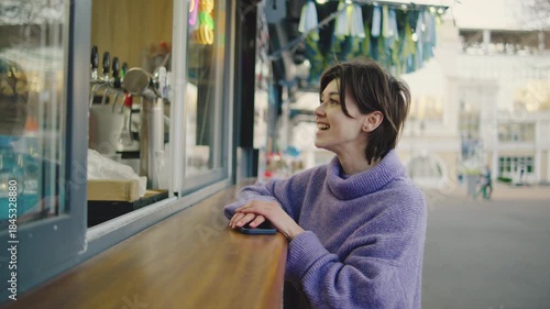 Woman smiles at a food stand while waiting for her order in a busy outdoor area with colorful decorations