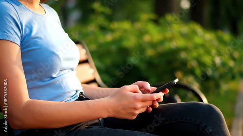 Youthful individual engaging with a smartphone while relaxing on a park bench, outdoor lifestyle perspective