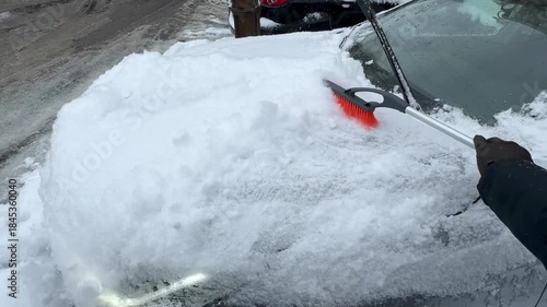 Manual snow removal from car hood using snow brush in winter, close-up video