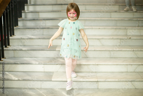Valokuva Caucasian girl walking down marble stairs in mint dress and white tights, facepa