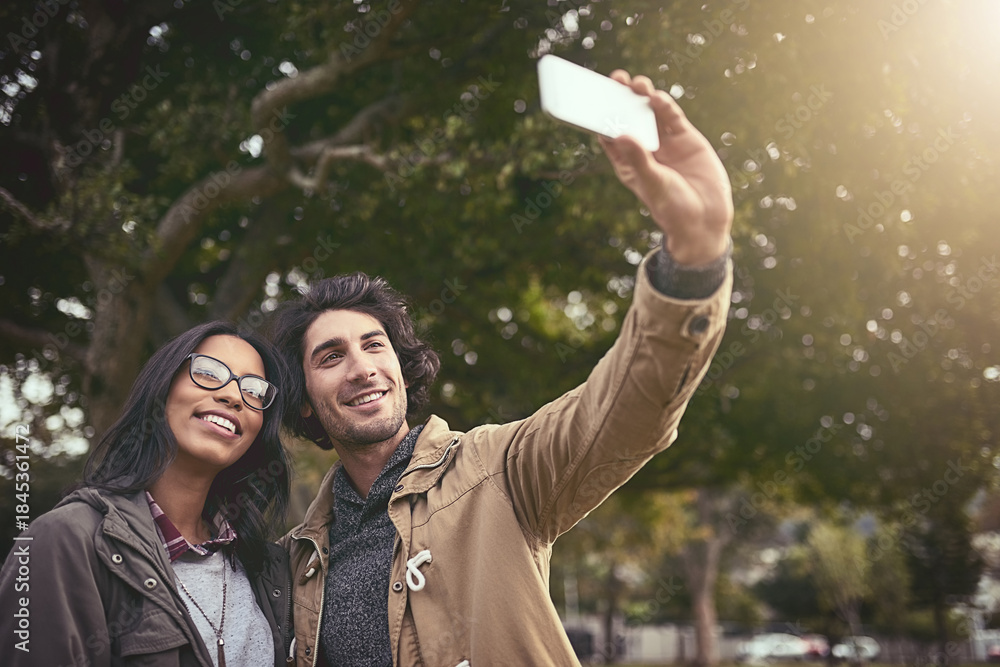 Fototapeta premium Couple, selfie and smile with love in park with care, bonding and adventure in spring on holiday. Interracial people, man and woman with hug, photography or memory on social network on app in Toronto