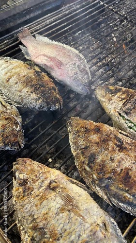 A whole tilapia, seasoned with salt and grilled over charcoal – a traditional Thai street food dish, fragrant with a rustic texture and authentic outdoor cooking style.