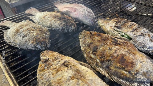 A whole tilapia, seasoned with salt and grilled over charcoal – a traditional Thai street food dish, fragrant with a rustic texture and authentic outdoor cooking style.