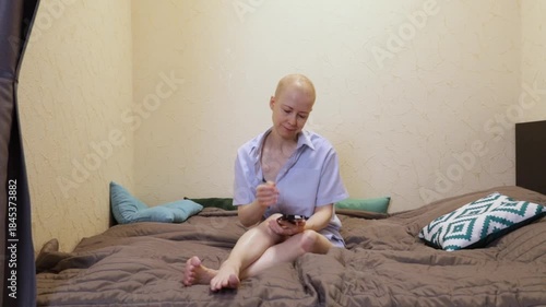 Female patient after chemotherapy lying on bed and browsing phone, concept of online shopping, independence, and rehabilitation