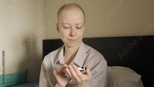 Bald woman after cancer therapy using smartphone indoors, concept of digital life, mindfulness, and emotional recovery.