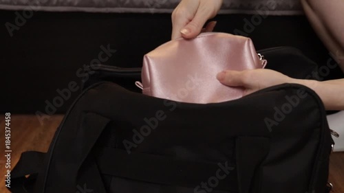 Close-up of woman’s hands packing a black travel bag at home, concept of organization, focus, and preparation for hospital or short trip.
