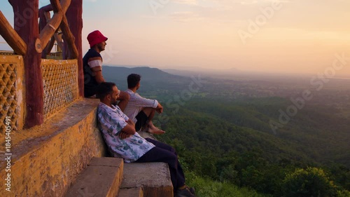 Three hikers trekking during sunset in the mountains under a partly cloudy sky, with a temple creating a breathtaking backdrop at Samai Mata Mandir, Banswara, near Udaipur, Rajasthan, India.