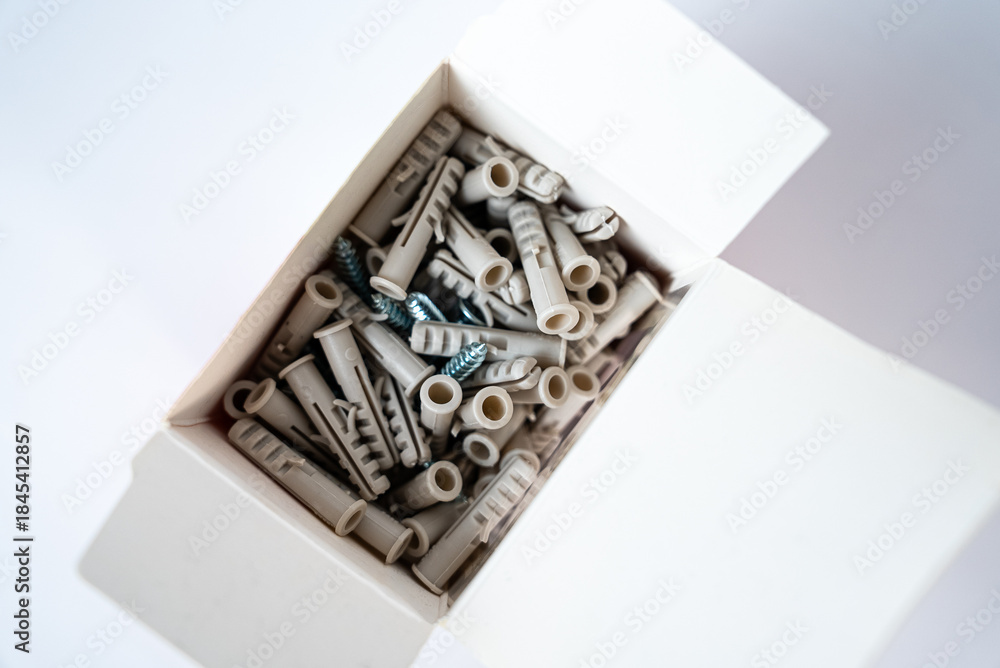 Fototapeta premium Open box filled with assorted wall plugs and screws on a white background. Construction and home repair supplies, hardware tools. High quality photo