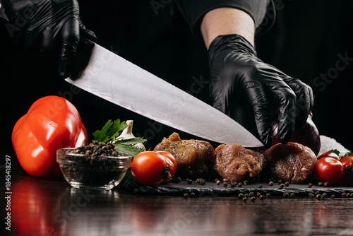 Fotografi Chef in black gloves skillfully slicing fresh vegetables and meat on a wooden cu