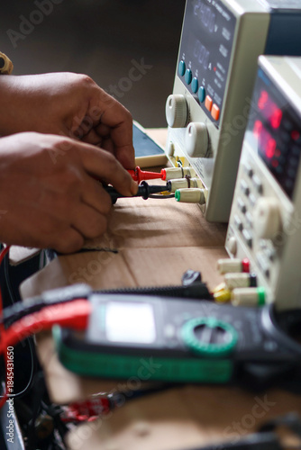 Hands connecting banana plugs to a laboratory DC power supply unit for testing and electronic troubleshooting.
