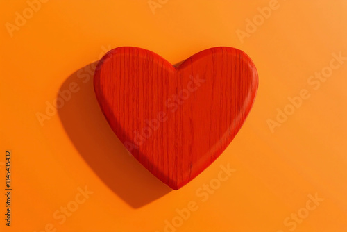 Red wooden heart casting a shadow on an orange background, symbolizing love and passion. Valentines day concept. Top view. 3d rendering.