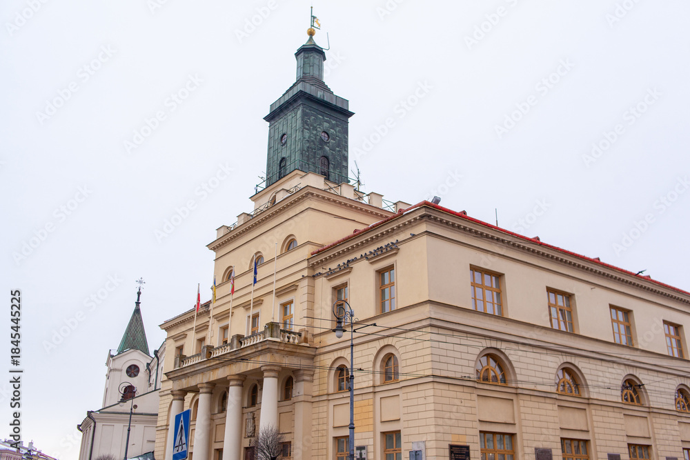 Fototapeta premium New City Hall in Lublin, Poland. A large building stands in the city center with a tall clock tower. Flags fly from the roof on a gray day in winter.