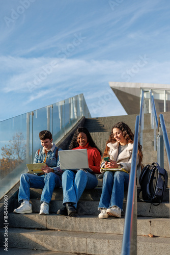 Multiethnic students using technology and notebooks while learning on college campus stairs
