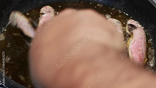 Red mullet are being fried in a pan.