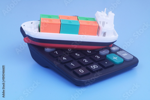Cargo ship with containers on black calculator on blue background. Sea ​​transportation budget and price concept.	