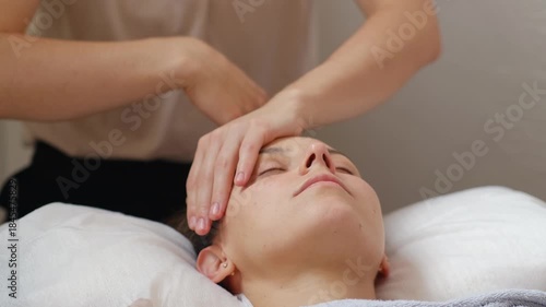 A woman is laying on a bed with her head resting on a pillow. A woman is massaging her face