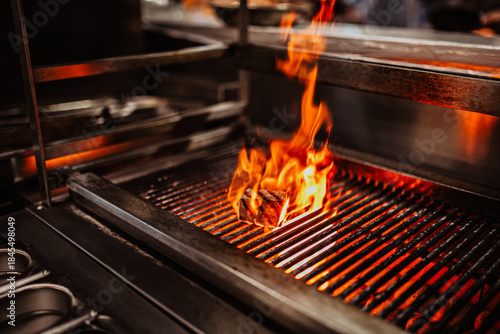 A close up shot of a delicious meat grilled in a restaurant kitchen with bright flames coming out of it