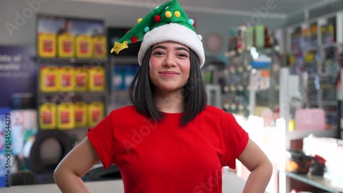 Cheerful young woman wearing a funny christmas hat smiling and giving a thumbs up in a car parts store
