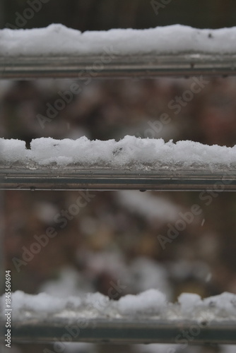 A close-up shot of thick, fresh snow resting on the metal railing of an outdoor structure during a snowy day.