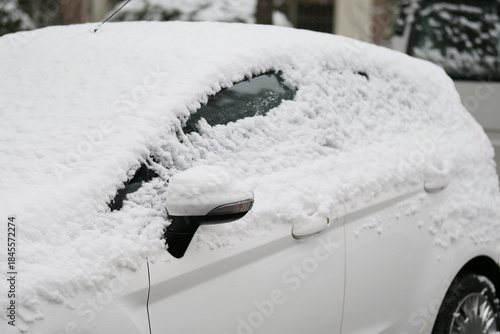 A close-up shot of a car heavily covered in fresh, wet snow on a winter day.