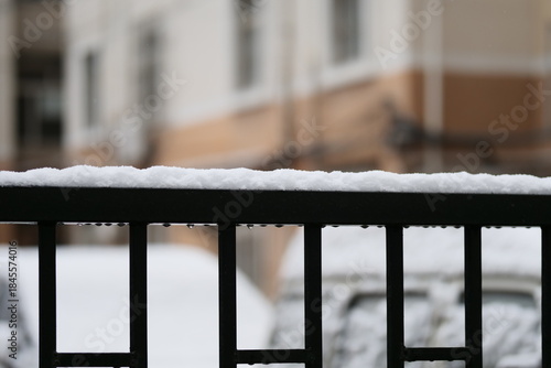 A close-up shot of thick, fresh snow resting on the metal railing of an outdoor structure during a snowy day.