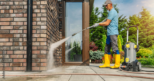 Man Uses Pressure Washer on Brick Wall During Sunny Day