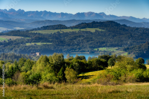 Scenic summer view of the tatra mountains and czorsztyn lake in poland, featuring lush green forests, rolling hills, and castle ruins in the distance