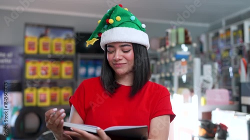 Young woman wearing a festive christmas hat while working and writing in a notebook inside a store