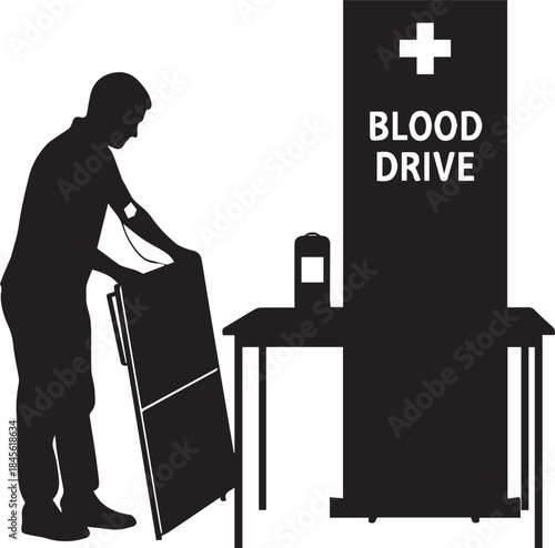 Silhouette of person setting up a blood drive station with signage and table