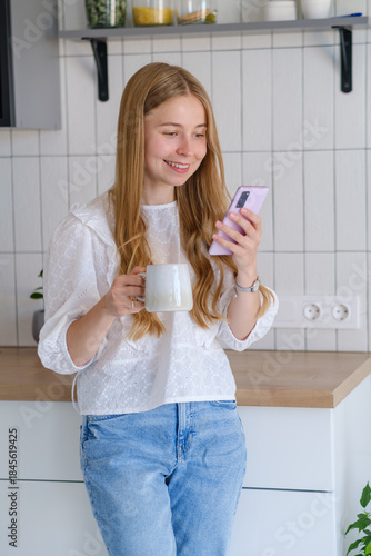 A girl uses a mobile phone in her kitchen at home. Freelance work, communication, business, communications, mobile applications, online meetings. City liaison worker.