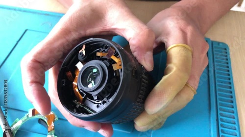 technician is disassembling a DSLR lens at his workshop desk. Close up