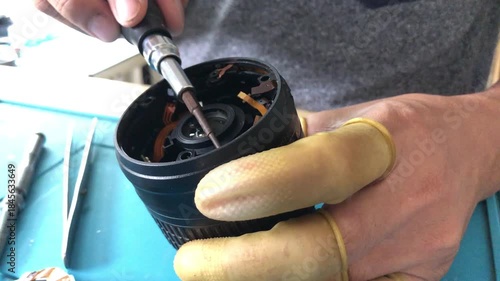 technician is disassembling a DSLR lens at his workshop desk. Close up
