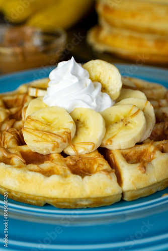 A golden waffle is topped with sliced bananas, whipped cream, and a warm peanut butter drizzle on a blue plate in Waukesha County.