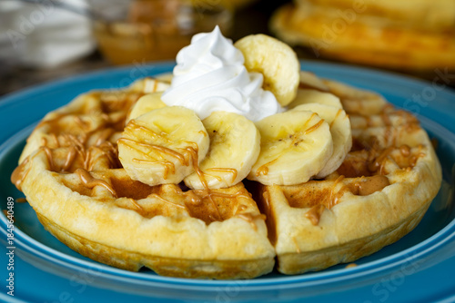 A golden waffle is topped with sliced bananas, whipped cream, and a warm peanut butter drizzle on a blue plate in Waukesha County.