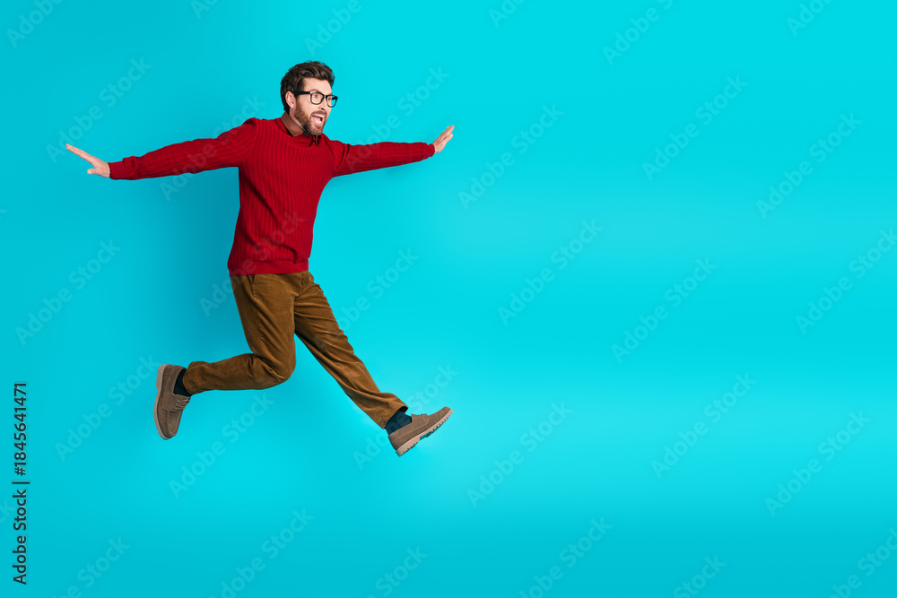 Fototapeta premium Young man in red sweater leaps with outstretched arms against blue background energy joy and lifestyle for advertising fashion and lifestyle projects