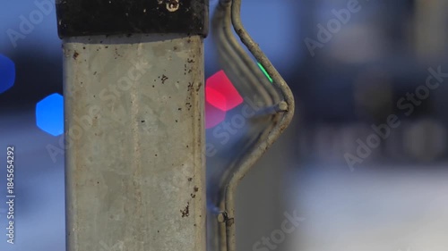 Close-up of a Metal Bollard or Post with Hexagonal Bokeh Lights in the Background - Urban Night Scene Detail Focusing on a Grungy Metal Post and Blurred Colorful Traffic Signals