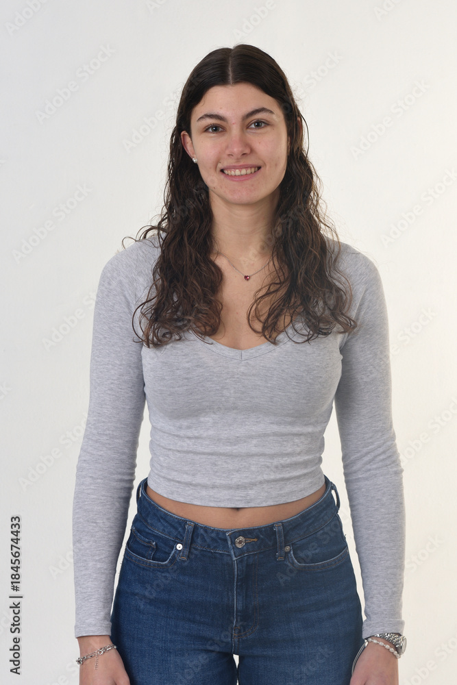 Obraz premium waist up front view portrait of an 18-year-old girl, looking at the camera and smiling with teeth on a white background.