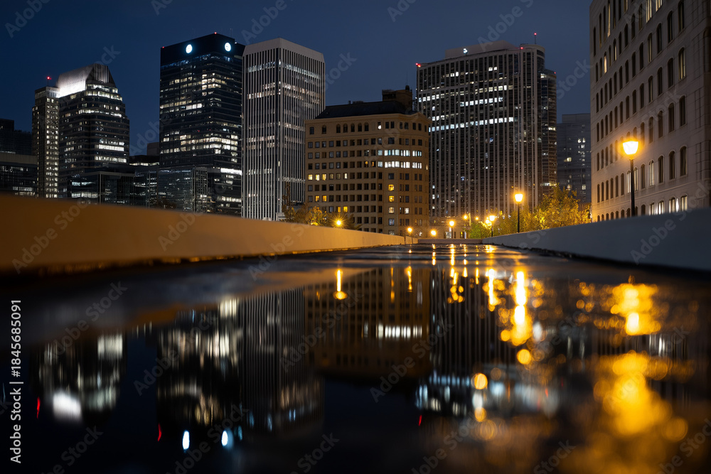 Naklejka premium A stunning urban skyline is beautifully illuminated at night, with reflections on wet streets capturing the essence of city life, vibrancy, and modern architecture.