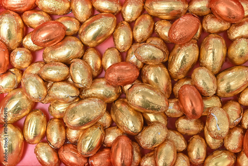 Large and small gold, orange and bronze foil wrapped chocolate easter eggs, against a peach orange background.