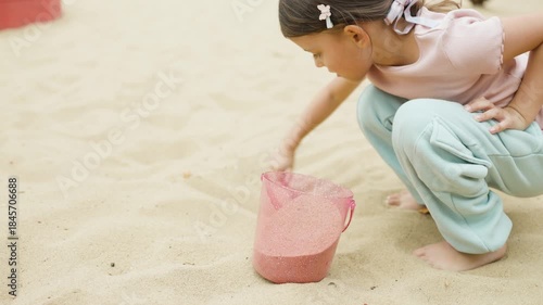 A girl plays in a sandbox on a playground in a park