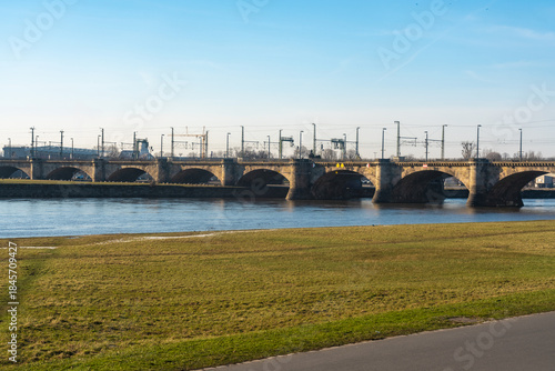 View of the Marine bridge over the serene river under the clear sky, with green grass adding a splash of color, in Dresden, Saxony, Germany.