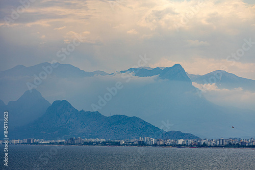 Fototapeta Naklejka Na Ścianę i Meble -  Dramatic panoramic view of Antalya city under moody cloudy skies, with mountains and coastline meeting the dark sea. Antalya, Turkey, Mediterranean.

