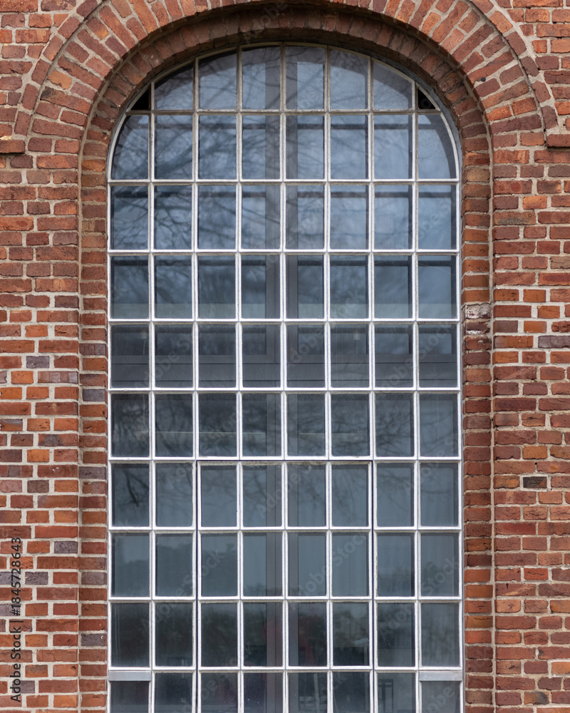 Obraz premium Brick building features large arched window with grid pattern and reflective surface in urban setting
