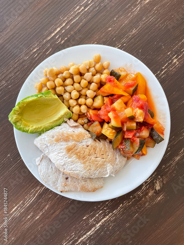 Fried chicken fillet served with stewed vegetables chickpeas and avocado as healthy balanced lunch. Nutritious meal with protein fiber and plant fats for everyday eating