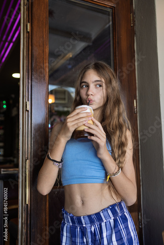 Young preteen girl enjoying a cold coffee beverage outdoors in summer in Santorini, Greece, 4 October 2025